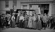 Photo of a group of suffragettes holding banners watched by bystanders: link to Project 1